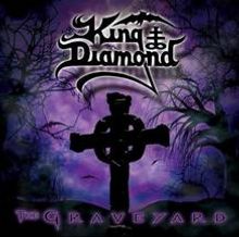 "King Diamond", "The Graveyard": Dunkle Silhouette eines Kreuzes vor violettem, nebligem Hintergrund, kahles Geäst.
