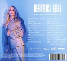 BEATRICE EGLI – HÖR NIE AUF DAMIT 2.0. Eine Frau in einem hellen Anzug posiert, lächelt und blickt zur Seite.