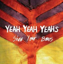 "Yeah Yeah Yeahs Show Your Bones" steht in weißer Schrift über abstrakten, farbigen Stoffmustern in Rot, Lila und Gelb.