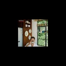 Niall Horan, Dinner Party. Ein Mann sitzt in einer Küche, trinkt aus einer Tasse. Fenster und Geschirr im Hintergrund.