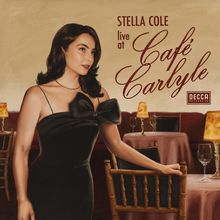 "Stella Cole live at Café Carlyle." Eine stilvolle Frau in einem eleganten schwarzen Kleid in einem gemütlichen Café.