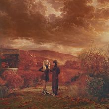 Zwei Personen stehen in herbstlicher Landschaft, umgeben von rötlichen Blättern. Dramatischer Himmel mit dichten Wolken.