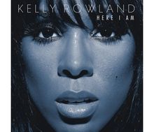 Text: „KELLY ROWLAND HERE I AM“. Nahaufnahme eines Gesichts mit feuchter Haut, offenem Mund und intensiven Augen.