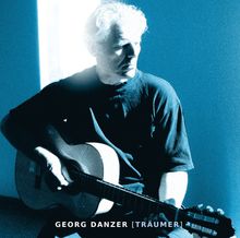 "GEORG DANZER [TRÄUMER]". Ein Mann sitzt und spielt Gitarre im blauen Licht.