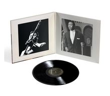 Der Text "CHESS" ist auf einem schwarzen Vinyl zu sehen. Eine Schallplattenhülle mit Schwarz-Weiß-Fotos enthält die Platte.