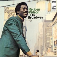 "Reuben Wilson On Broadway" in grüner und schwarzer Schrift. Ein Mann in einem grünen Anzug lächelt auf einer belebten Straße.