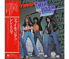 Japanische Texte links; "Thin Lizzy" Logo oben. Drei Männer in Jeans posieren stark vor städtischer Kulisse.