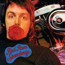 Text: "Red Rose Speedway". Ein Mann mit einer roten Rose im Mund steht vor einem Motorrad.