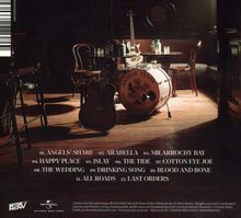 Trackliste: ANGELS' SHARE, ARABELLA, MILARROCHY BAY. Bar mit Gitarren und Schlagzeug. Dämmerige Beleuchtung.
