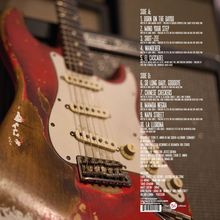 Texte auf der rechten Seite: Tracklisten für Side A und B mit Titeln wie "Born on the Bayou" und "La Llorona". Im Hintergrund eine abgenutzte, rot-weiße E-Gitarre.