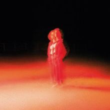 Keine erkennbaren Texte. Eine Figur in roter Beleuchtung steht unscharf in einer dunklen Umgebung.