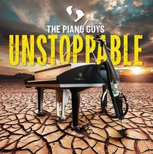 "THE PIANO GUYS UNSTOPPABLE" in gelber Schrift, Klavier und Cello auf trockenem Boden, Sonnenuntergang im Hintergrund.