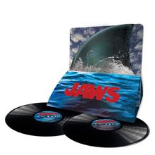 Der Text "JAWS" in roten Buchstaben auf blauem Hintergrund, zwei Schallplatten davor, Hai-Linie im Wasser.