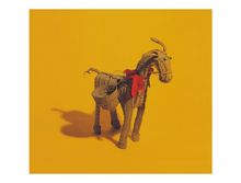 Strohfigur eines Esels mit roter Schleife, auf gelbem Hintergrund.