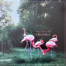 Text: "THE JULIES Cherisher". Mehrere Flamingos stehen auf grünem Gras vor dichtem Buschwerk.