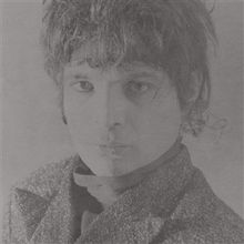 Das Bild zeigt ein Schwarz-Weiß-Porträt einer Person mit dunkler Frisur, die melancholisch in die Kamera blickt.