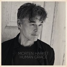 Text: "Morten Harket Human Grace". Schwarz-weißes Porträt eines nachdenklichen Mannes vor einer verwitterten Holztür.