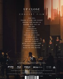 "Up Close" und "Concert Film" stehen oben, gefolgt von einer Liste von Songtiteln. Unten sind Musiker und Sänger auf der Bühne.