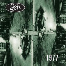Oben "ash." in einem ovalen Logo; unten "1977". Eine gespiegelte Straße mit umgekippten Mülleimern und Gebäuden.