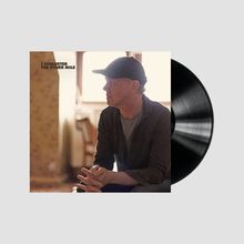 Text: "J SCHLUETER THE OTHER MILE". Eine Person mit Mütze sitzt nachdenklich in einem Raum, neben ihr eine Vinyl-Schallplatte.