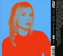 "Jazzinc" vertikal rechts, Frau vor blauem Hintergrund, rotes Haar und Kleidung, auffällige Ohrringe.