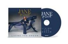 Texte: JANE, LIVING THE DREAM. Eine Frau in einem eleganten, blauen Outfit posiert mit einer fließenden Stoffbahn.