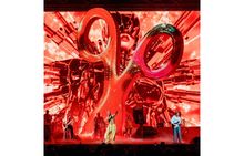 Die Zahl "20" in großen, glänzenden Buchstaben dominiert die Bühne. Musiker spielen vor einem roten, futuristischen Hintergrund.
