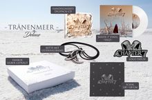 "TRÄNENMEER Deluxe" oben, diverse Fanartikel auf sandigem Hintergrund: CD, Vinyl, Kette, Box, Patch und Schal.