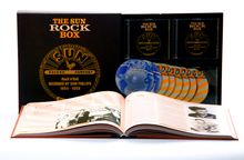 "The Sun Rock Box" ist auf einer Box und mehreren CDs zu sehen. Ein aufgeschlagenes Buch zeigt Fotos und Text.
