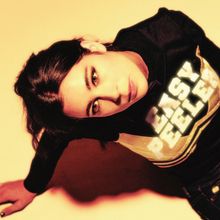 Der Text „EASY PEELER“ leuchtet auf einem Oberteil. Eine Person blickt intensiv und schräg von unten in die Kamera.