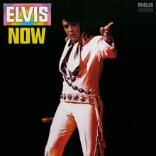 Text: "ELVIS NOW". Ein Mann in einem weißen Anzug zeigt mit ausgestrecktem Arm. Oben ein Logo.