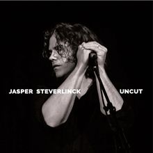 Texte: "JASPER STEVERLINCK UNKUT". Ein Mann mit lockigem Haar singt in ein Mikrofon, schwarz-weiß.