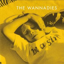 Text: "THE WANNADIES", "be a girl". Ein Kind liegt mit geschlossenen Augen, entspannt, im gelben Licht.