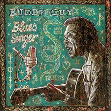 Text: "Buddy Guy", "Blues Singer". Darstellung eines Musikers mit Gitarre und Mikrofon vor grüner, reich verzierter Kulisse.