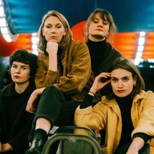 Vier Frauen in Herbstkleidung sitzen entspannt. Der Hintergrund ist bunt beleuchtet. Keine sichtbaren Texte.
