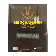 "Die Schamanin" in gelber Schrift, ergänzt durch einen Erläuterungstext. Oben Zähne, angeordnet in Form eines Tierschädels.