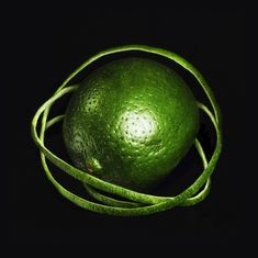 Keine Texte vorhanden. Eine grüne Limette mit spiralförmig abgelöster Schale auf dunklem Hintergrund.