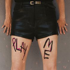 "PLAY ME" steht auf den Schenkeln einer Person in schwarzen Ledershorts geschrieben.