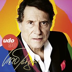 „udo 90“ in einem roten Kreis, darunter eine große Unterschrift. Ein älterer Mann in Anzug, bunter Hintergrund.