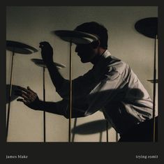 "james blake", "trying 2021"; Ein Mann balanciert mehrere Teller auf Stäben in einem dunklen Raum.