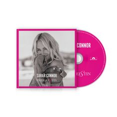 „SARAH CONNOR FREI GEISTIN“. Pinkfarbene CD und Cover, Schwarzweißfoto einer lächelnden Frau in Jeansjacke.