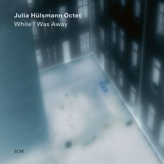 Text: "Julia Hülsmann Octet While I Was Away." Eine verschwommene Ansicht eines Innenhofs mit beleuchteten Fenstern.