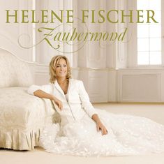 Text: "HELENE FISCHER Zaubermond". Eine Frau in einem weißen Kleid sitzt auf einem eleganten Sofa in einem hellen Raum.