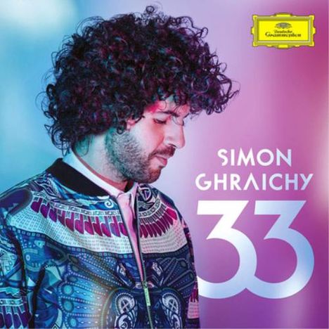 Text: "Simon Ghraichy 33". Ein Mann mit lockigem Haar in bunter Jacke, vor pastellfarbenem Hintergrund.