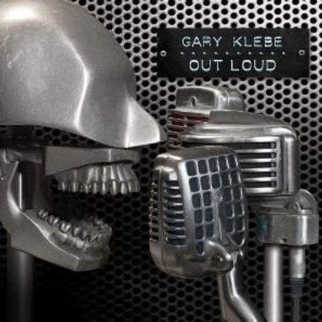 Text: "GARY KLEBE OUT LOUD". Ein Metallschädel und mehrere Mikrofone vor einem perforierten Hintergrund.