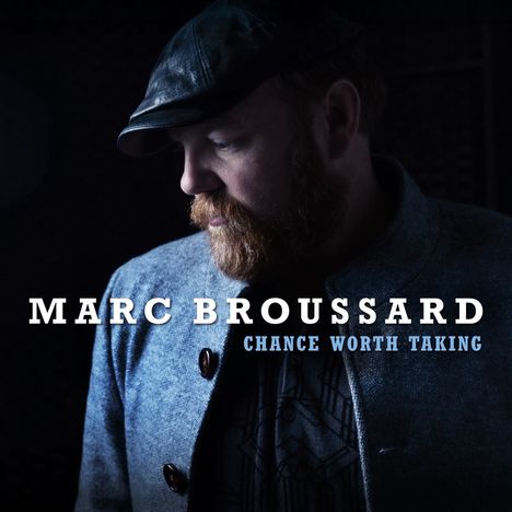 Text: "MARC BROUSSARD, CHANCE WORTH TAKING". Ein Mann mit Bart, trägt Hut und Mantel, schaut nach unten, dunkler Hintergrund.