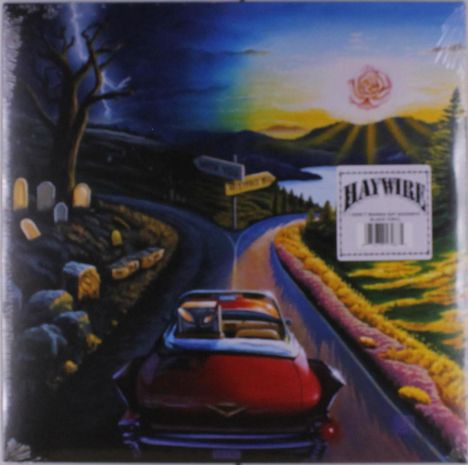 Text: "Haywire". Illustration: Ein rotes Auto auf einer Straße bei Sonnenuntergang, links ein Friedhof, rechts Blumen.