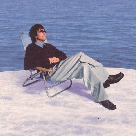 Keine Texte vorhanden. Eine Person sitzt entspannt in einem Klappstuhl auf Schnee vor einem See im Hintergrund.