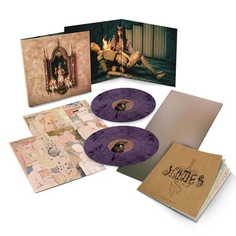 Text: "HADES LYRIC BOOK". Zwei lila Schallplatten mit einem Cover, das eine Puppe zeigt, umgeben von Kerzen. Kunstwerke liegen daneben.