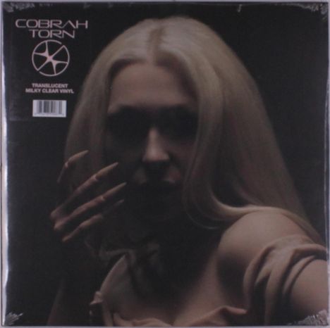 „COBRAH TORN“ oben links, darunter ein stilisiertes Symbol. Eine Person mit langen Haaren ist im dunklen Hintergrund.